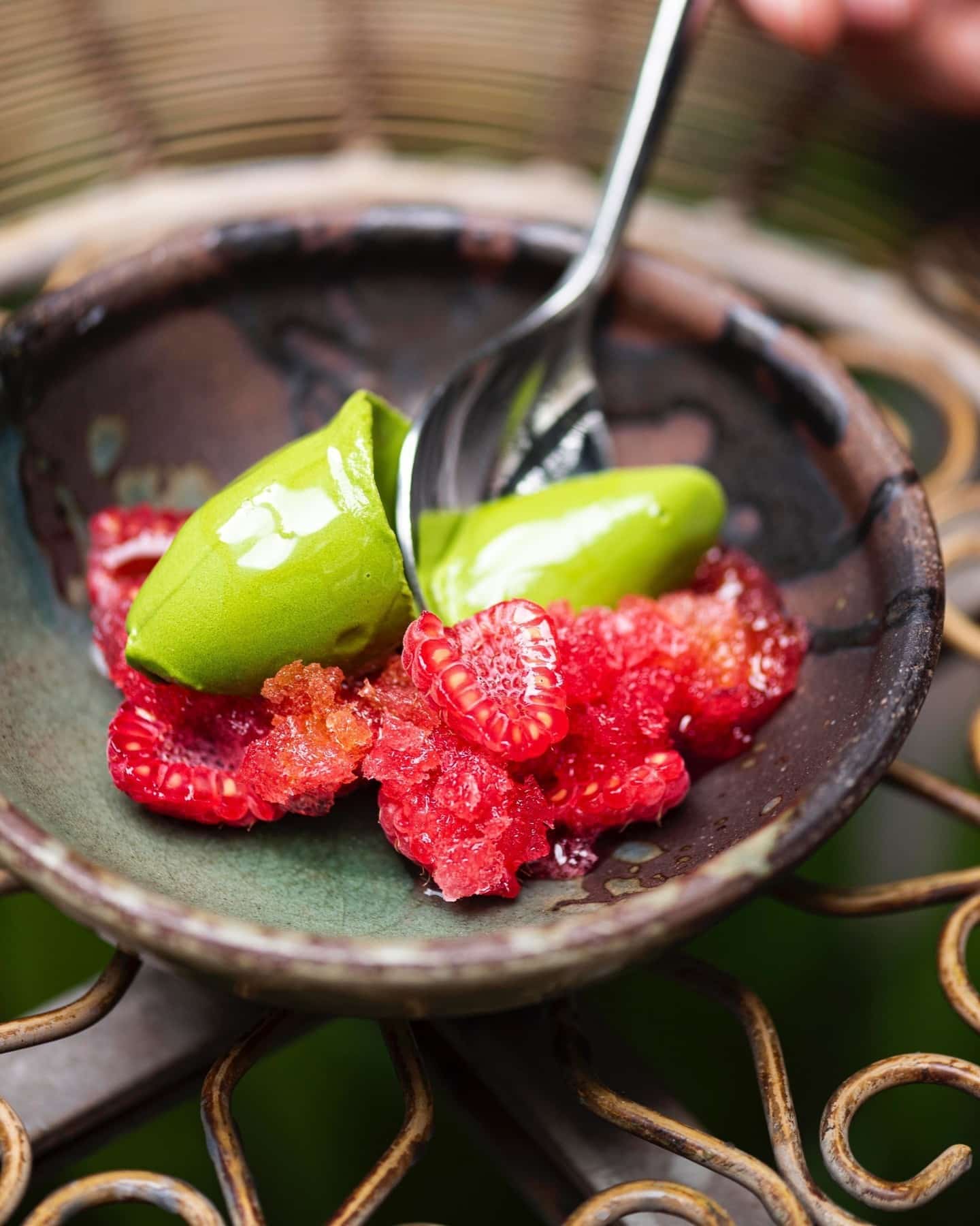 Green matcha dessert with raspberries on a dark plate, with a spoon ready to serve.